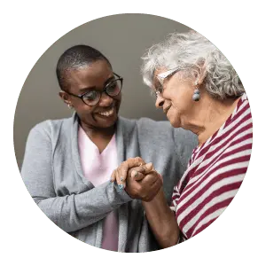 Female caregiver helping senior woman and holding her hand.