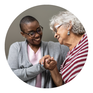 Female caregiver helping senior woman and holding her hand.