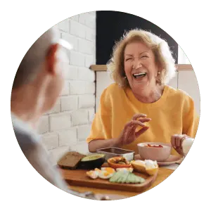 Image of senior woman eating at table and laughing.