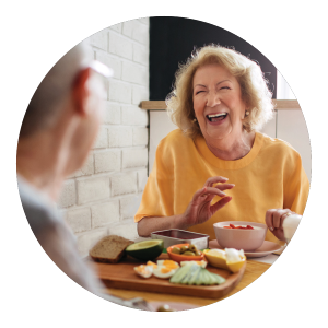 Image of senior woman eating at table and laughing.