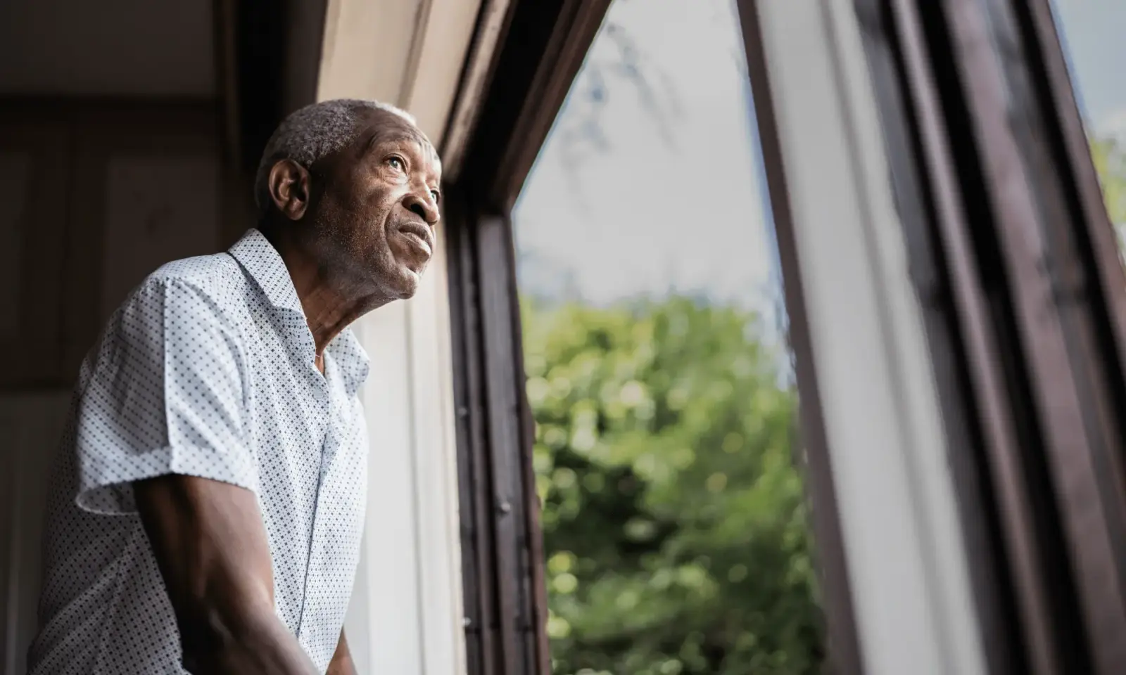 An older adult male living with dementia looks out the window.