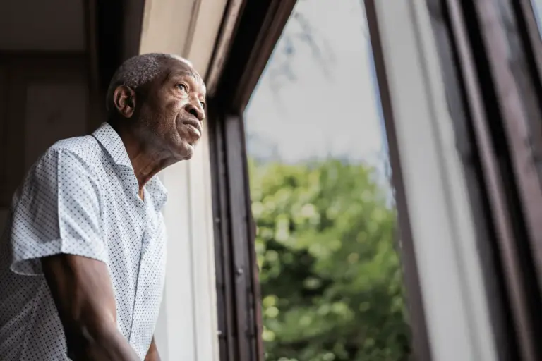 An older adult male living with dementia looks out the window.