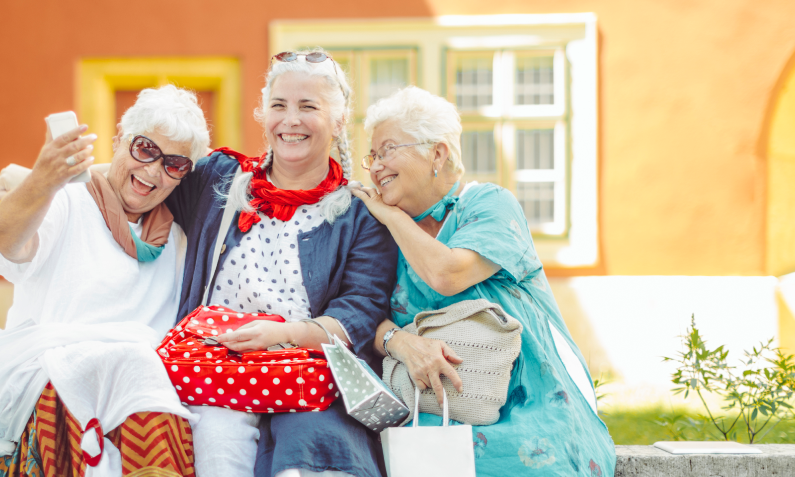 Three happy seniors pose for a selfie in front of a yellow background.