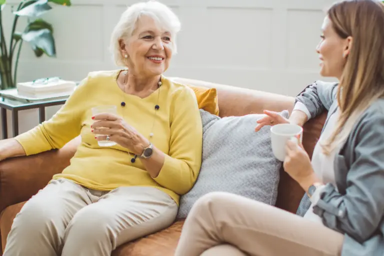 Adult woman holds a cup of coffee while chatting with an older woman about in-home respite care for dementia