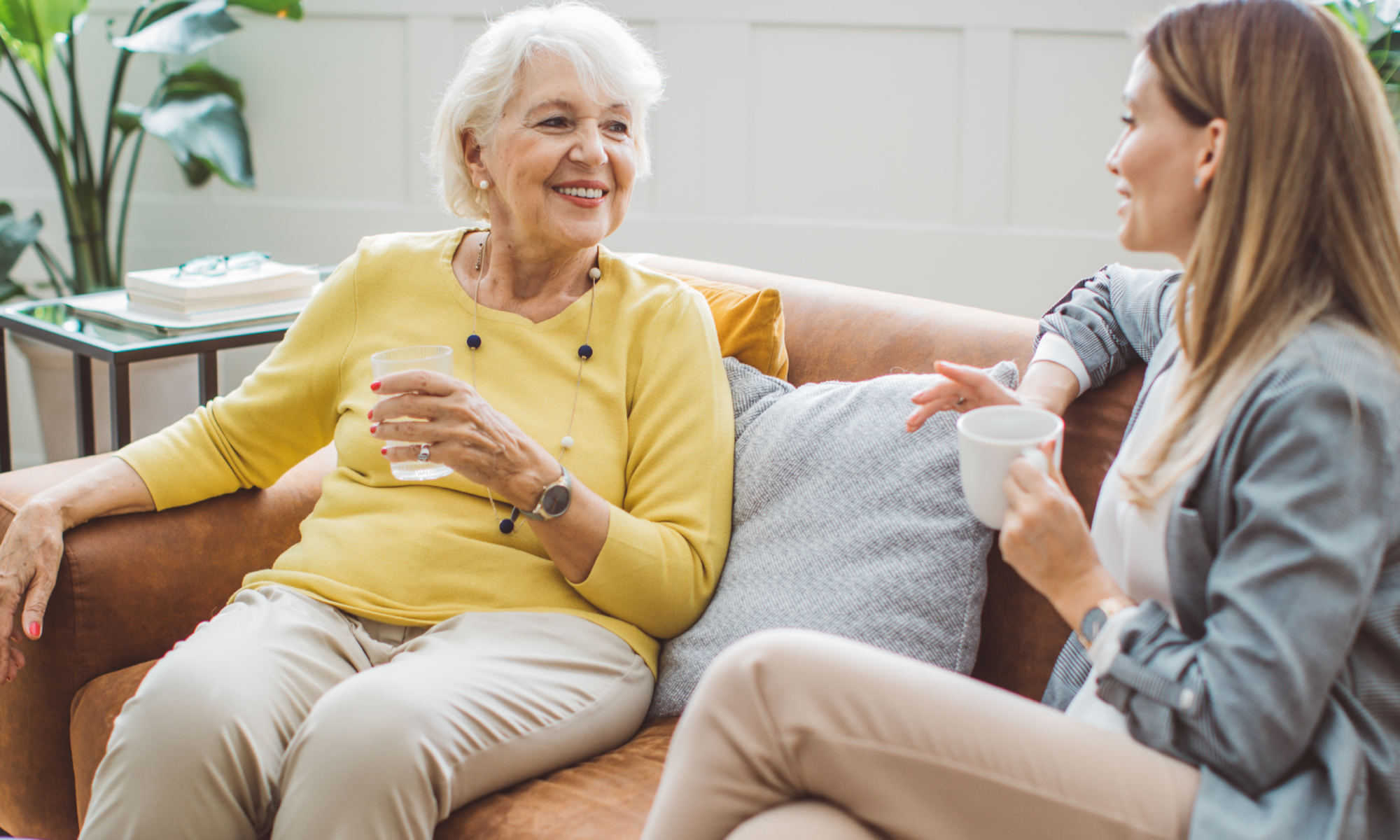 Adult woman holds a cup of coffee while chatting with an older woman about in-home respite care for dementia