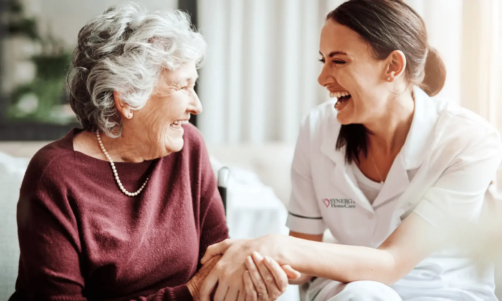 SYNERGY HomeCare caregiver laughs with an older woman who lives in an assisted living community.