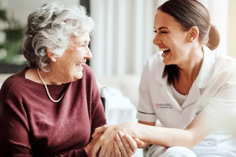 SYNERGY HomeCare caregiver laughs with an older woman who lives in an assisted living community.