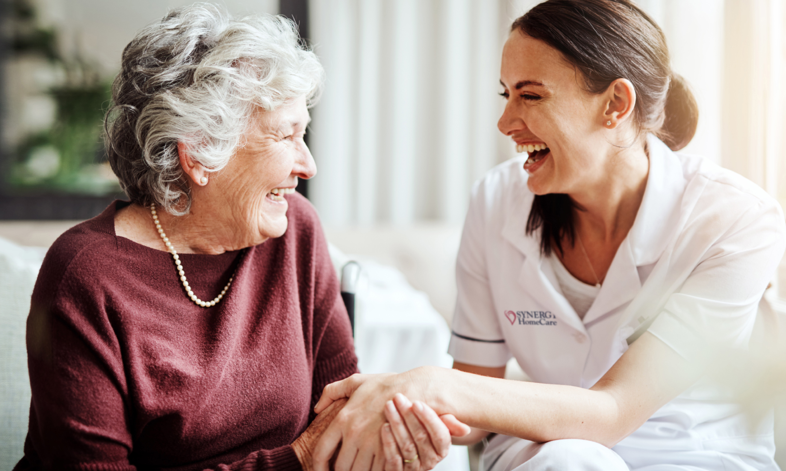 SYNERGY HomeCare caregiver laughs with an older woman who lives in an assisted living community.