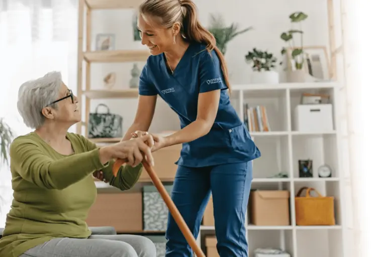 An older woman who uses a cane to ambulate is assisted by a SYNERGY HomeCare caregiver.