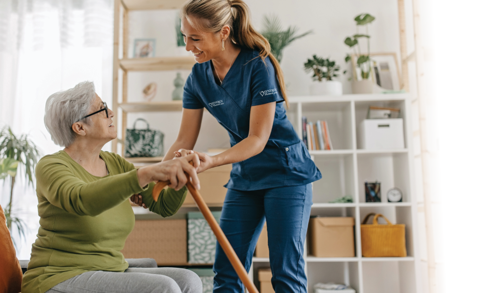 An older woman who uses a cane to ambulate is assisted by a SYNERGY HomeCare caregiver.