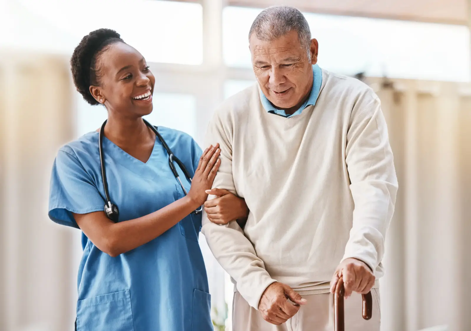 Smiling young woman caregiver supports senior man as he walks with a cane