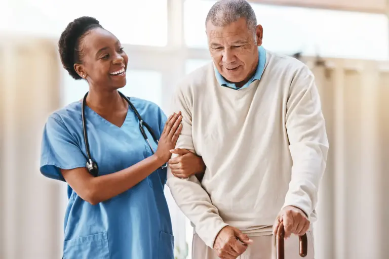 Smiling young woman caregiver supports senior man as he walks with a cane