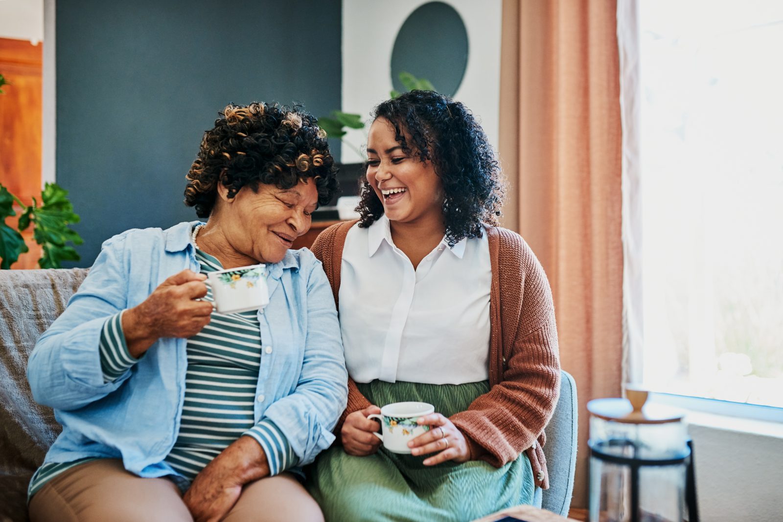 Shot of a young woman having coffee with her elderly relative on the sofa at home