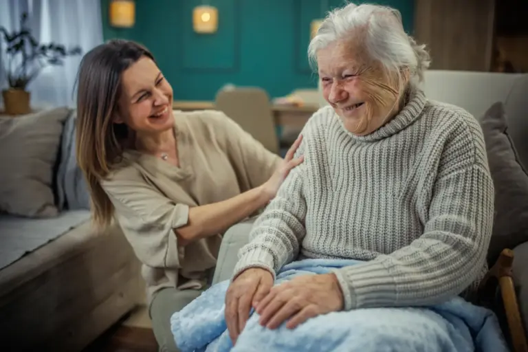 Cheerful adult woman smiling with senior mother during a check-in visit to her home.