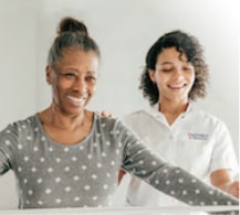 Caregiver assisting a senior woman with her balance activities and smiling.