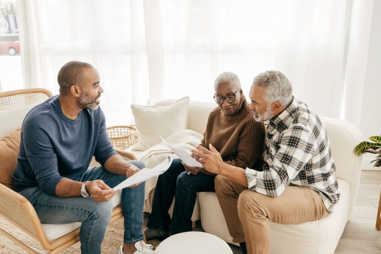 A son and husband sit with a senior woman as they discuss advanced care planning and help her draft her will.