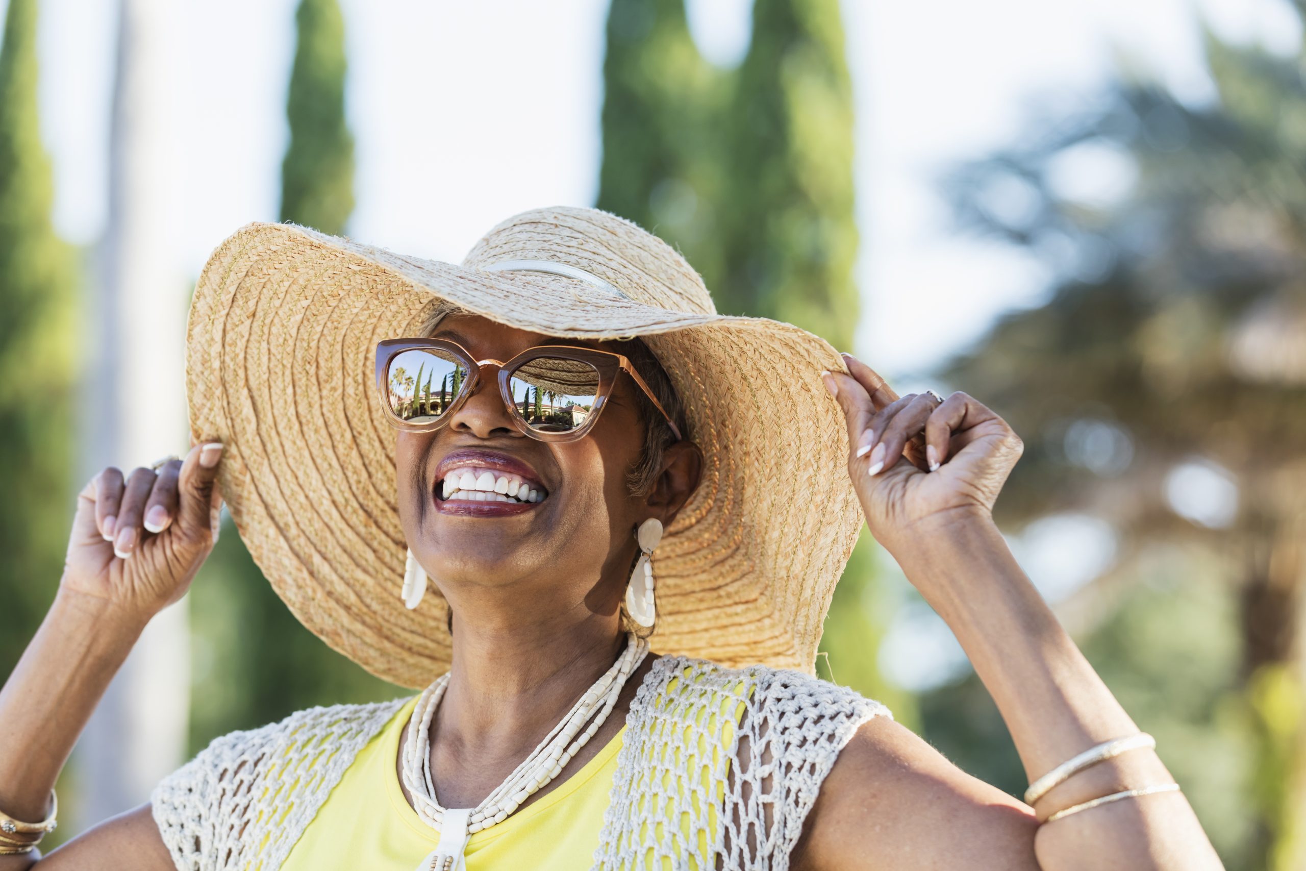 Senior woman with sunhat and sunglasses smiling outside on a sunny day.