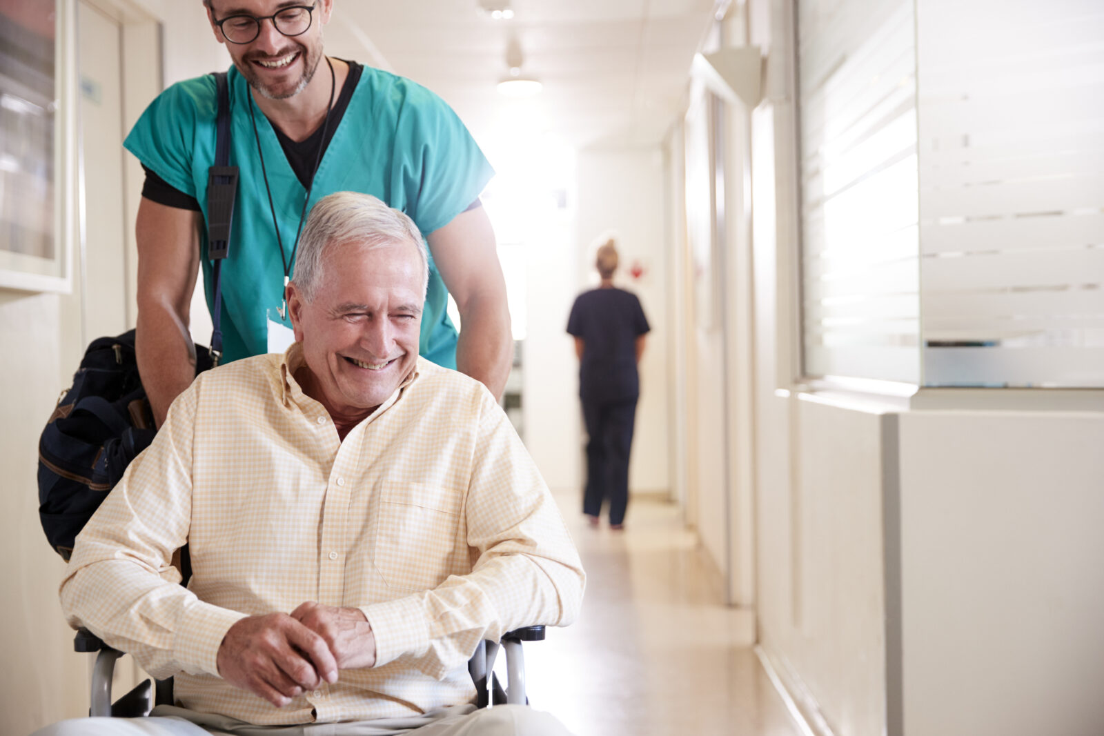 Male Orderly Pushing Senior Male Patient Being Discharged From Hospital In Wheelchair