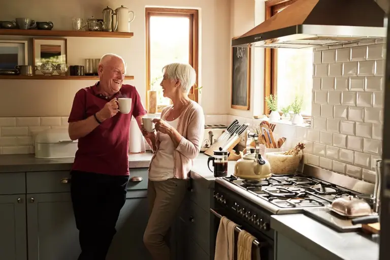 Older couple enjoys coffee together in their kitchen and discuss at home dementia care safety.