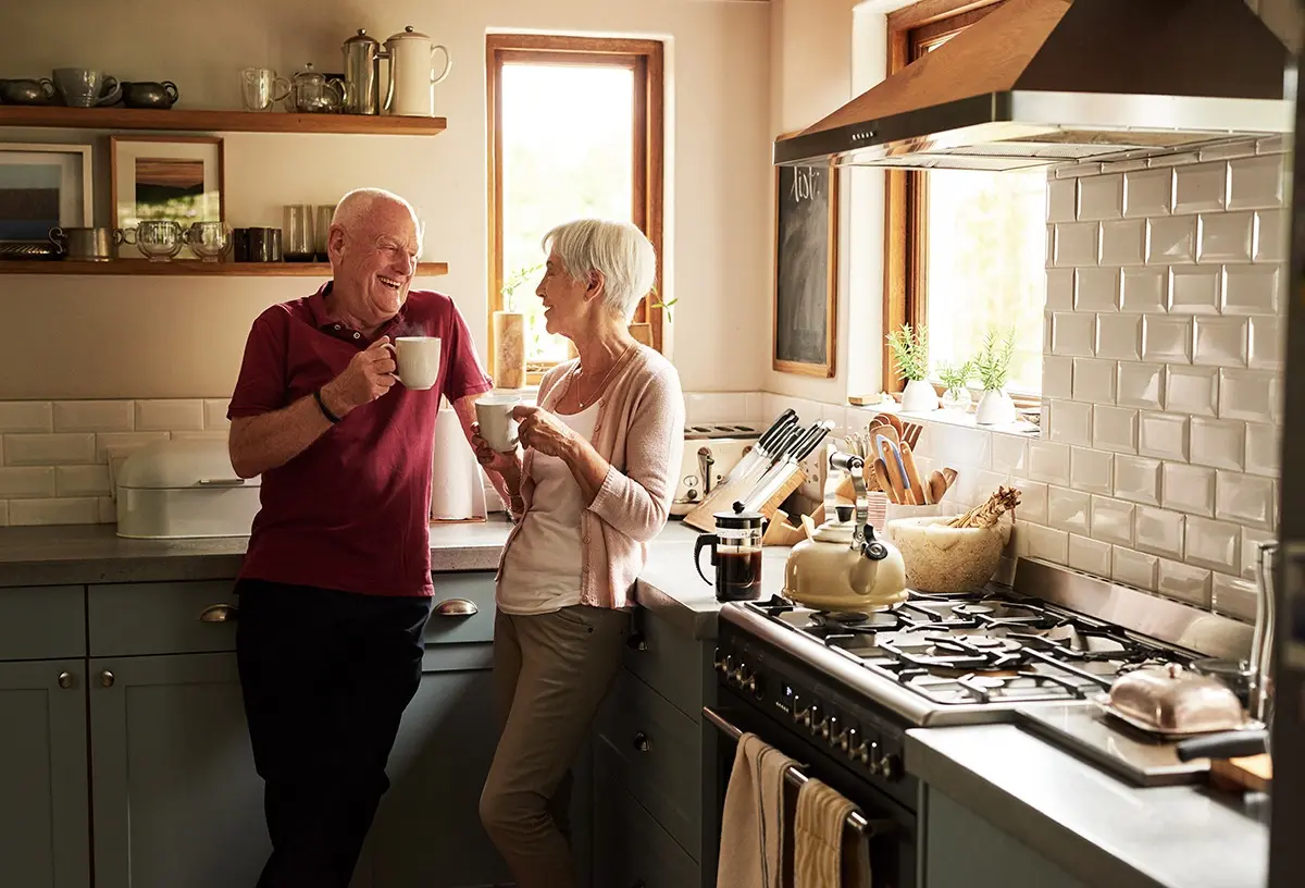 Older couple enjoys coffee together in their kitchen and discuss at home dementia care safety.