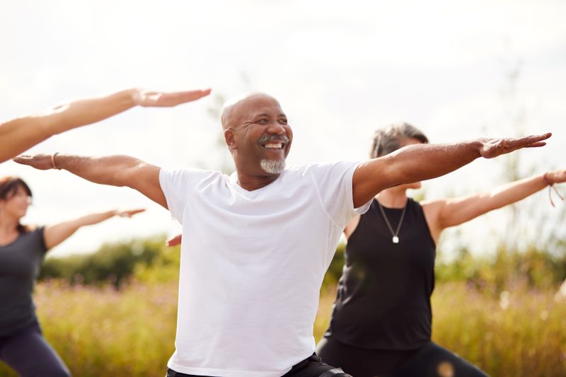 Smiling man does yoga with others in an outdoor meadow