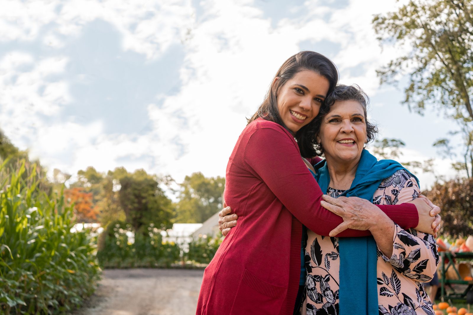 Smiling middle-aged woman hugs smiling senior woman on a sunny day outside, showcasing stress reduction programs.