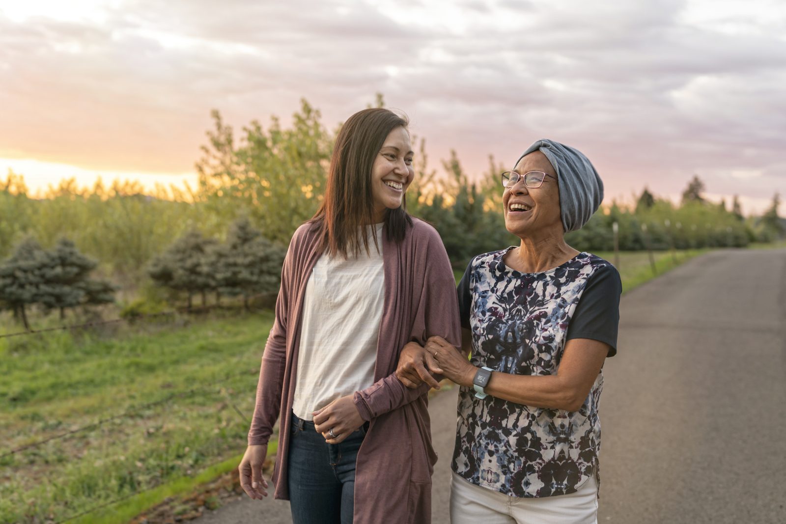 Senior woman and middle aged woman walk down a rural street, smiling and interlinking arms
