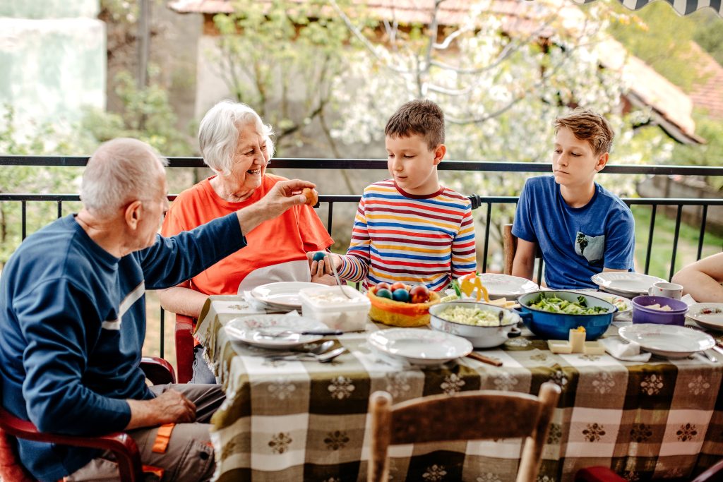 A senior couple eats dinner with their children and grandchildren outside.
