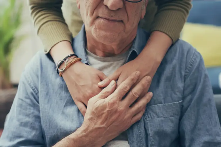 Senior man rested in a seated position while receiving an embrace from behind