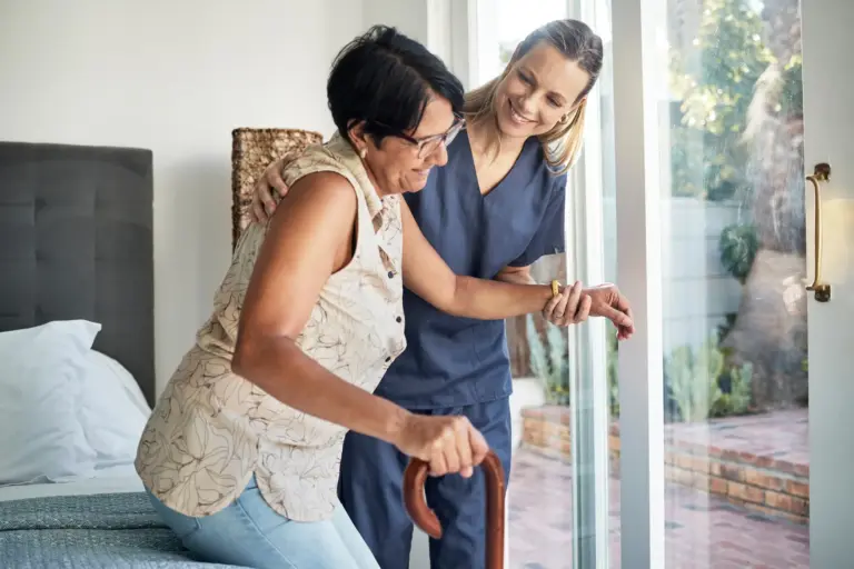 SYNERGY HomeCare caregiver helping senior get out of bed.