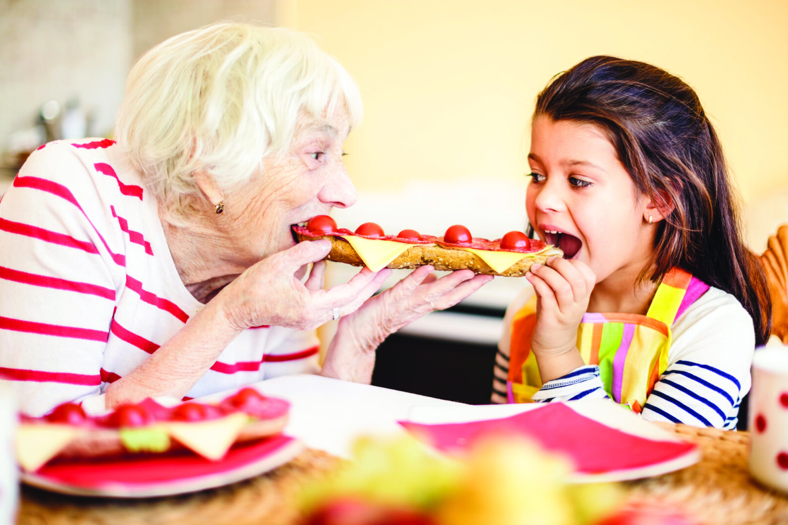 Grandmother eating sandwich with granddaughter.