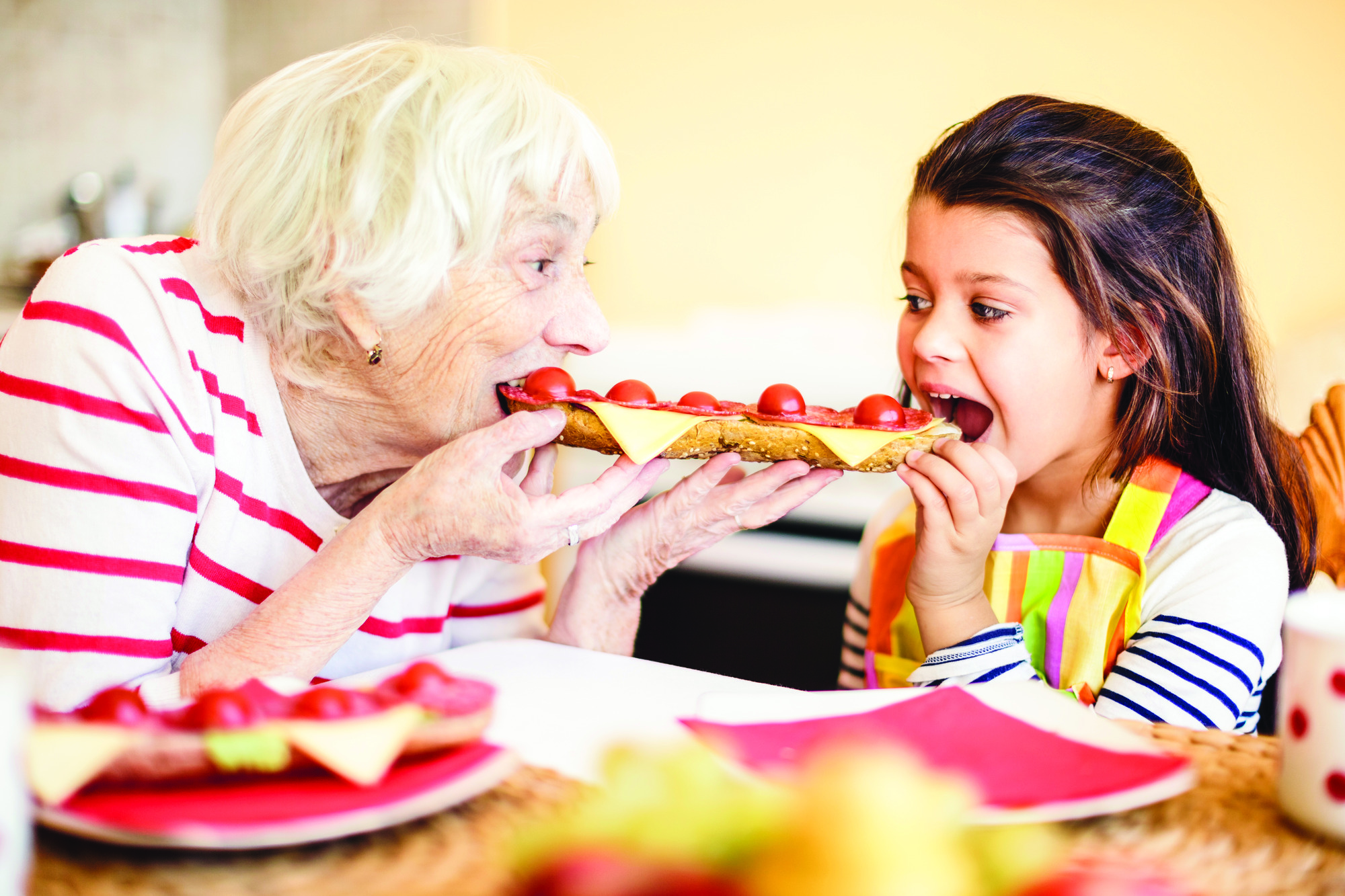 Grandmother eating sandwich with granddaughter.