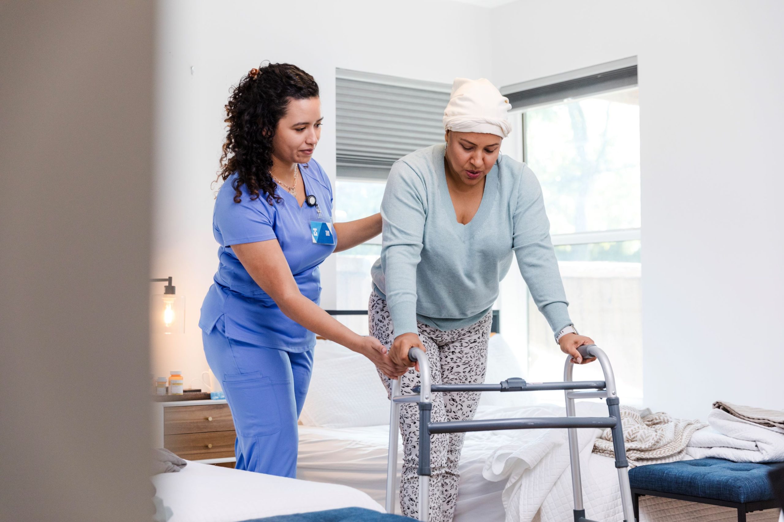 Middle-aged woman practicing fall precautions with a walker and caregiver assistance in her bedroom