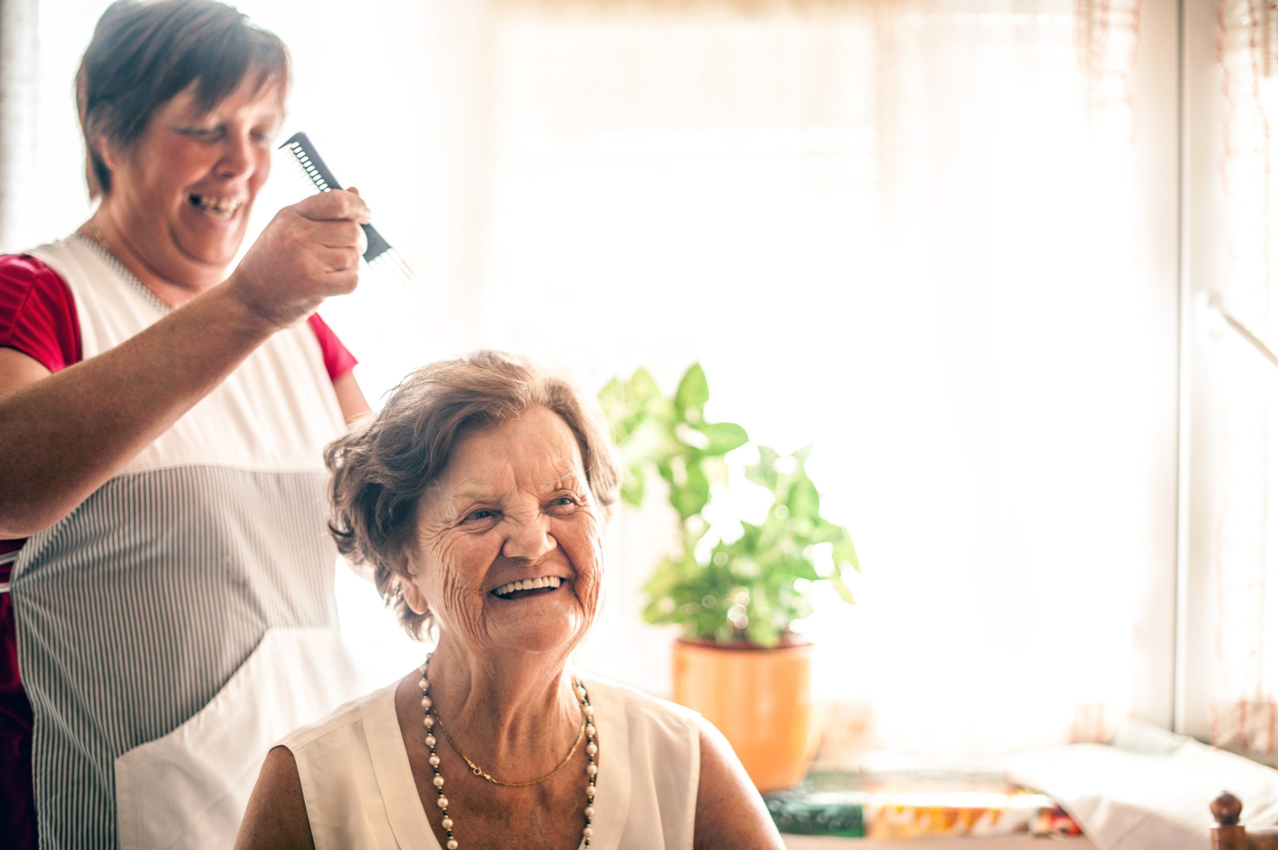 A SYNERGY HomeCare caregiver visits with a senior client living with Parkinson’s, assisting her with getting dressed and making sure that her hair is combed.