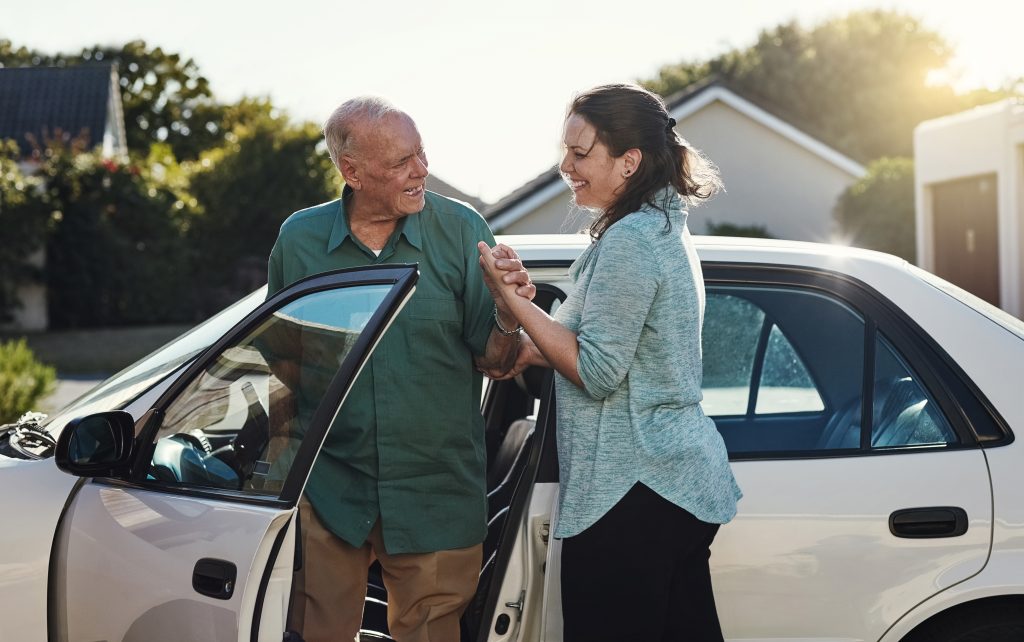 A SYNERGY HomeCare caregiver assists a senior in getting out of the car following an appointment.