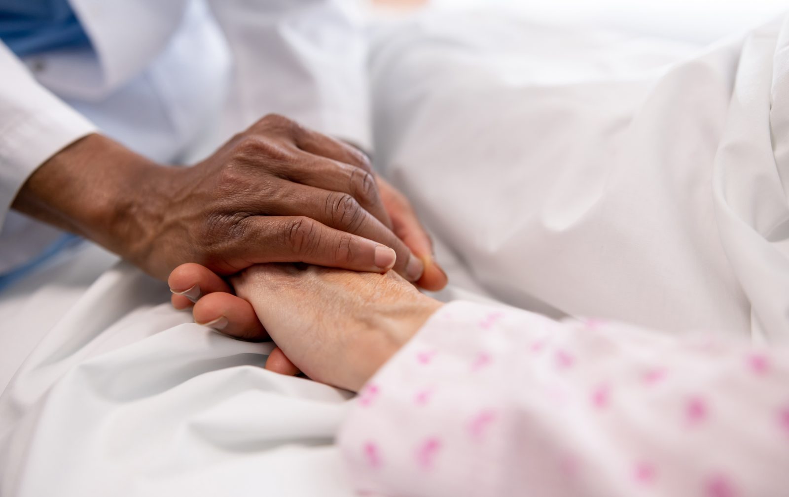 Close-up on a caregiver holding the hand of a woman in bed.