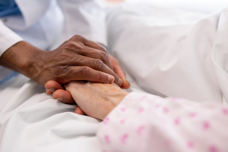 Close-up on a caregiver holding the hand of a woman in bed.