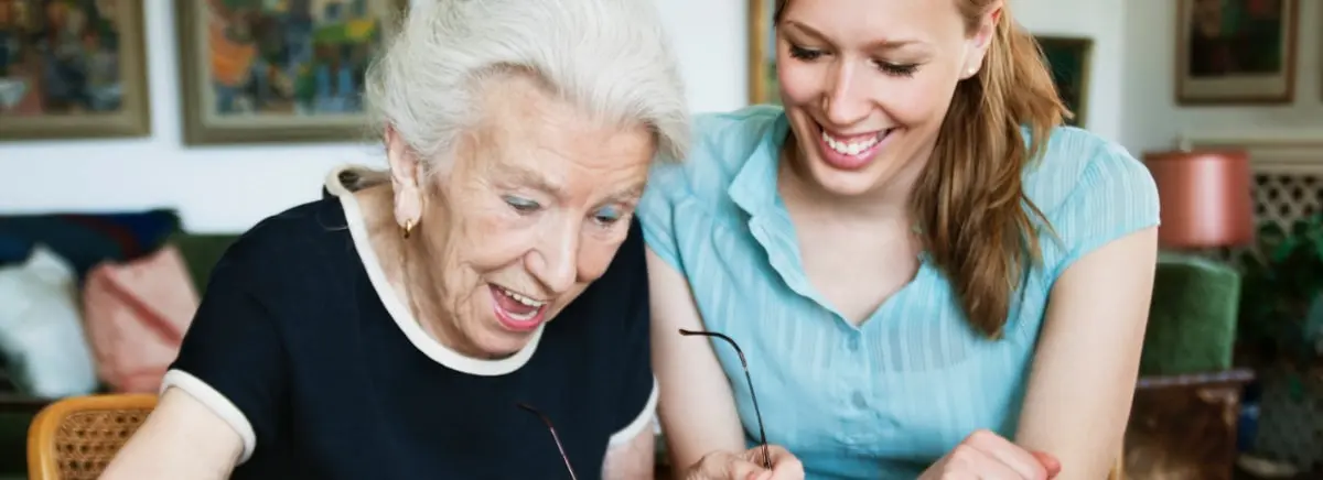 Senior woman having fun with her caregiver and doing a crossword puzzle together as an enriching activity.