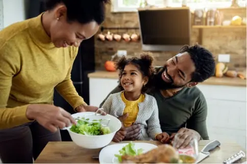 Young family sitting down at the dinner table getting ready to eat and smiling.