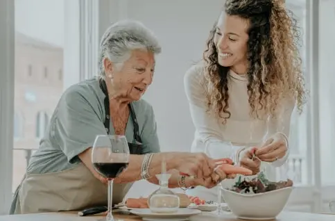 Senior woman preparing a salad with her younger female caregiver.