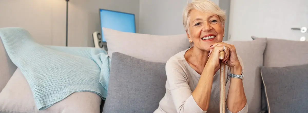 Senior woman sitting on the couch holding her cane