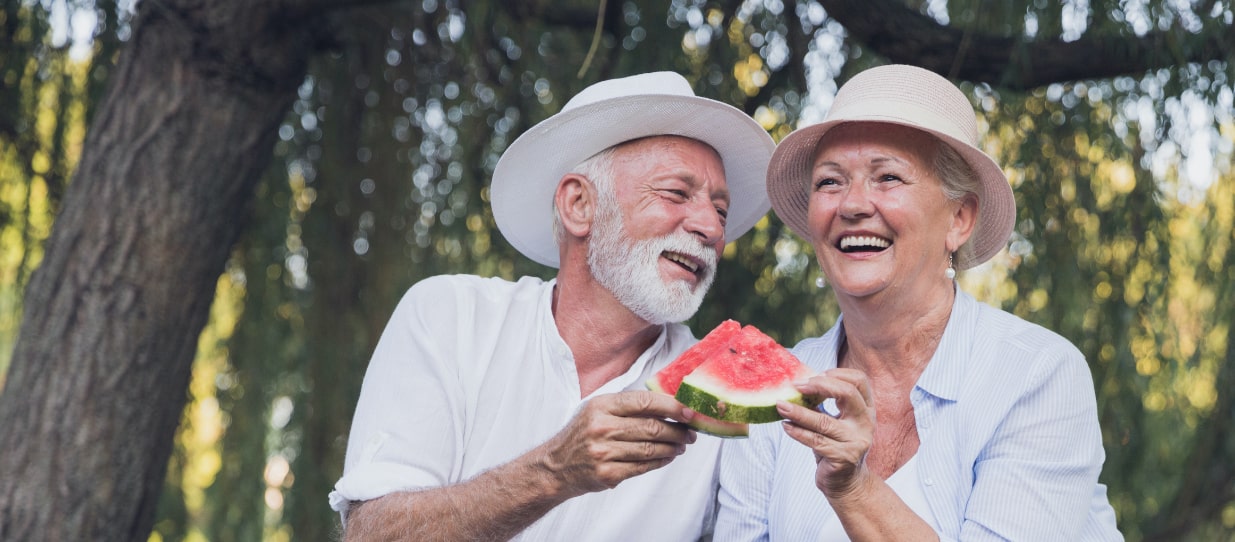 Senior man and woman having a picnic in the park and eating a slice of watermelon.