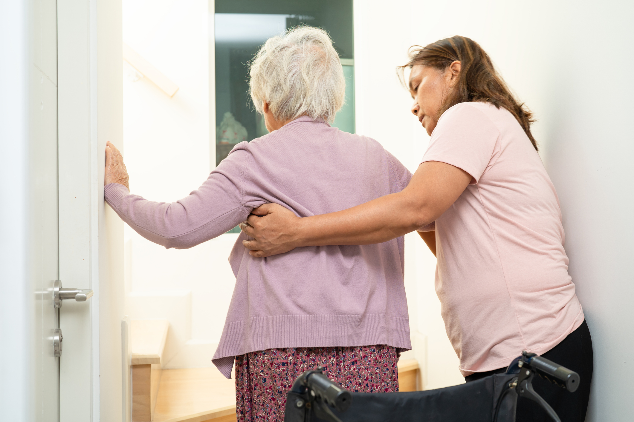 Caregiver assisting senior woman with Parkinson’s safely move from wheelchair into home bathroom