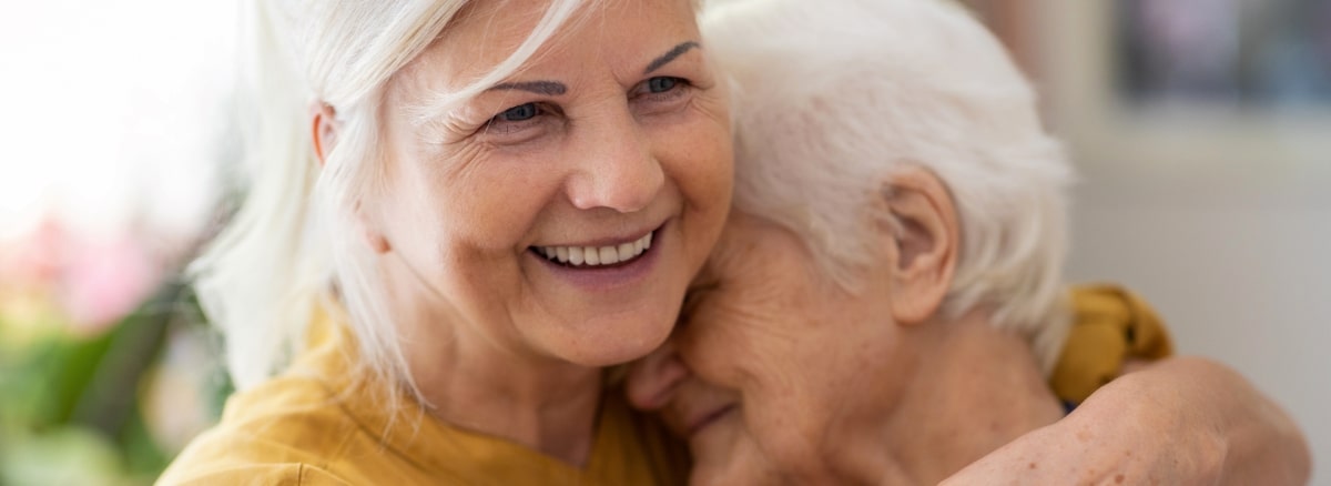 An Adult woman hugging her senior mother and smiling.