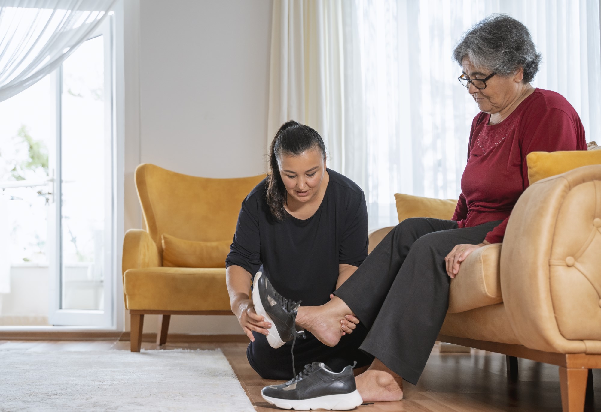 A caregiver assists a woman living with a disability in putting shoes on.