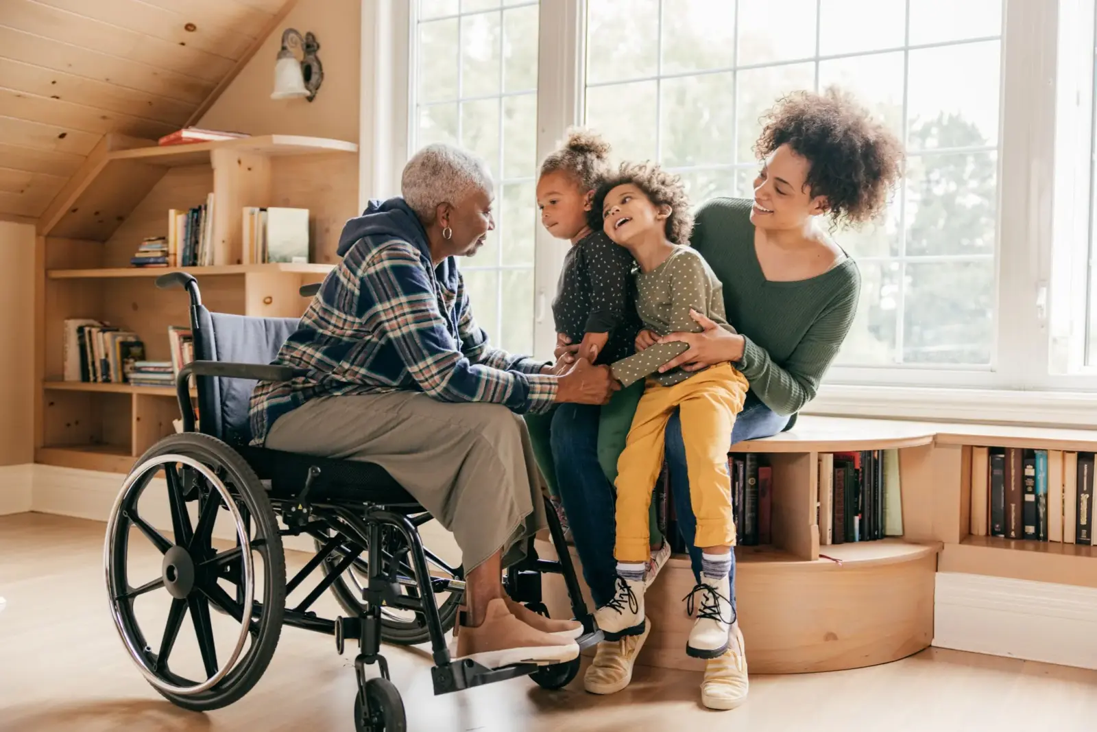 A smiling young woman holds her two children as they cheerfully visit their grandmother who is in a wheelchair.