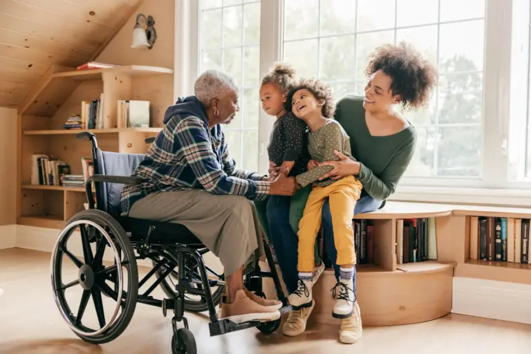 A smiling young woman holds her two children as they cheerfully visit their grandmother who is in a wheelchair.