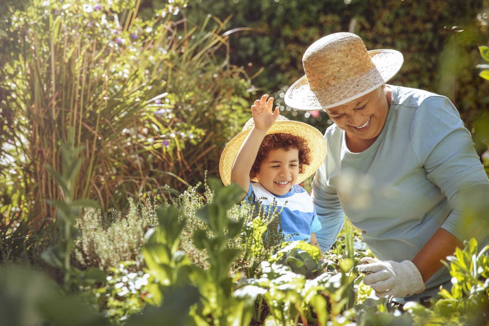 Grandmother and grandson in a sunny garden with hats and shade — summer safety for seniors.