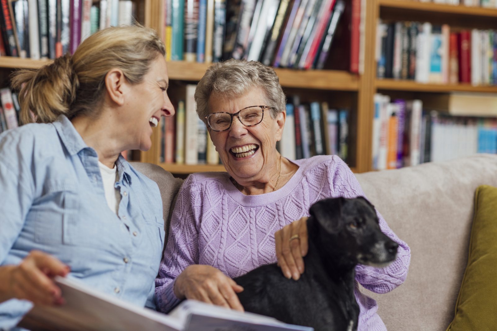 At-home companionship: daughter and senior mother sharing a photo album — aging in place with in-home support