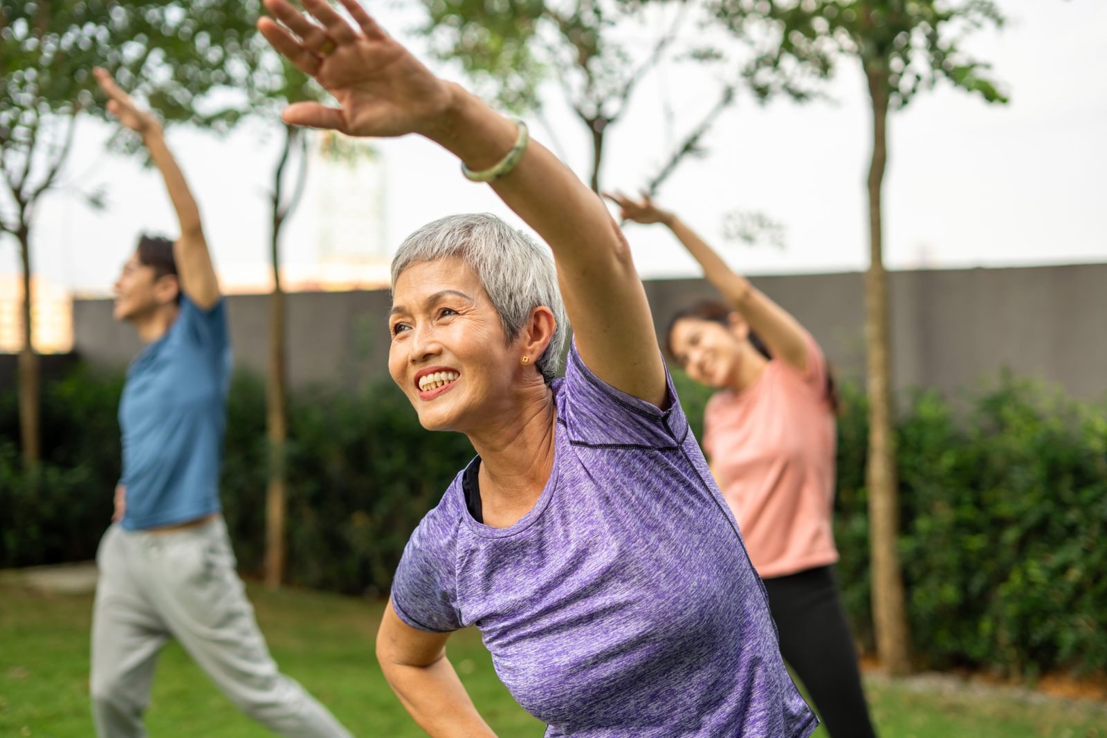 Senior woman outside in a group doing tai-chi exercises.